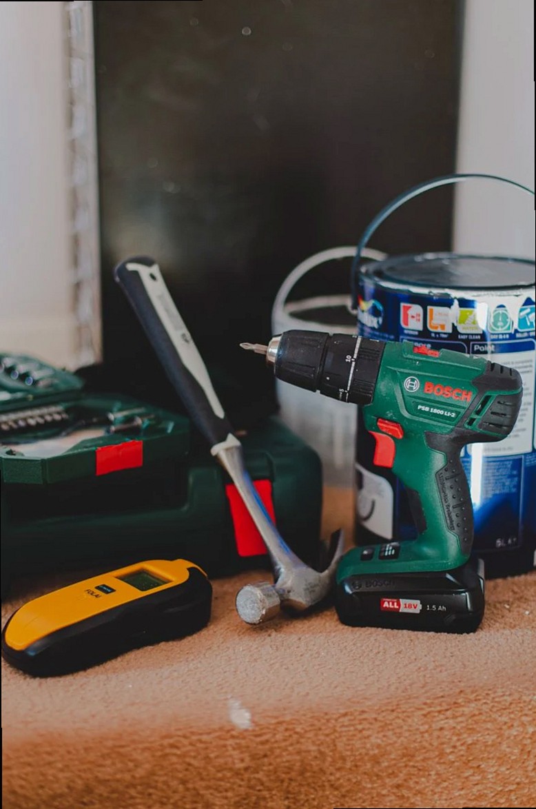 A selection of essential tools for home improvement projects, featuring a drill, hammer, and paint supplies.